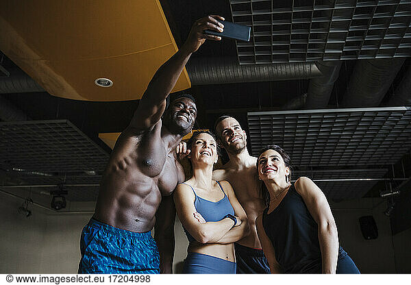 Lächelnde männliche und weibliche Athleten  die ein Selfie über ein Smartphone im Fitnessstudio machen