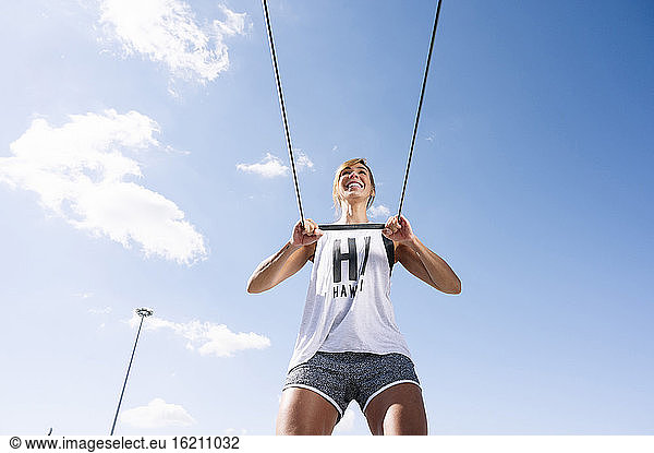 Lächelnde mittelgroße erwachsene Frau  die mit einem Gurt gegen den Himmel an einem sonnigen Tag trainiert