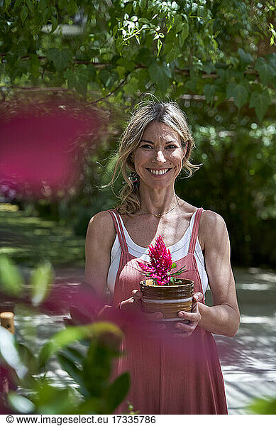 Lächelnde reife Frau stehend mit Blumentopf im Hinterhof