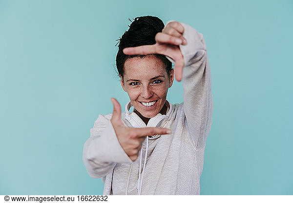 Lächelnde schöne Frau macht Rahmen mit den Fingern gegen türkisfarbenen Hintergrund