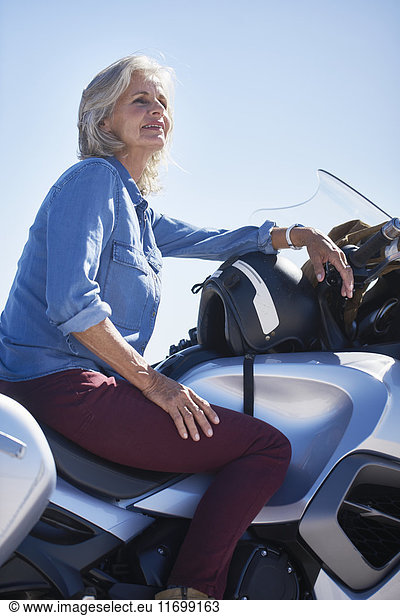 Lächelnde Seniorin auf dem Motorrad sitzend  wegschauend