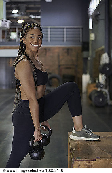 Lächelnde Sportlerin beim Heben von Kettlebells im Stehen im Fitnessstudio