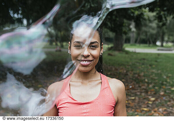 Lächelnde Sportlerin durch Seifenblase in öffentlichem Park gesehen