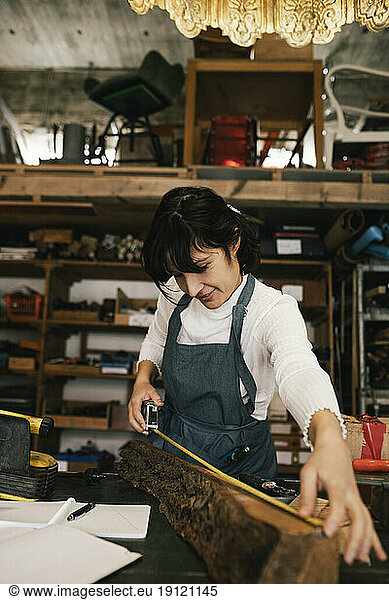 Lächelnde Unternehmerin misst Holz in der Upcycling-Werkstatt