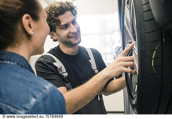 Lächelnder Automechaniker und Kunde betrachtet Reifen in der Werkstatt