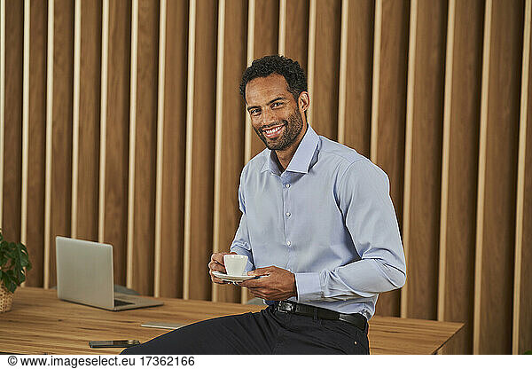 Lächelnder Geschäftsmann mit Kaffeetasse auf dem Konferenztisch