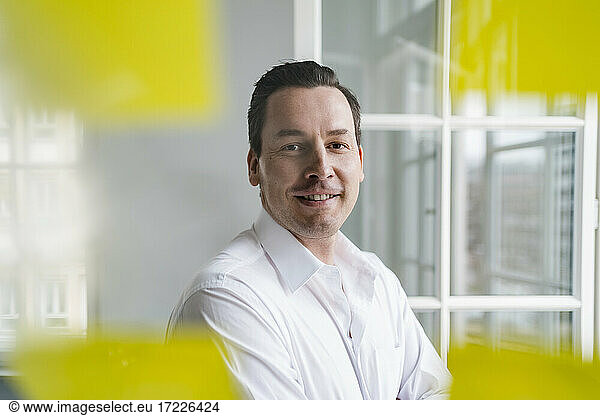 Lächelnder Geschäftsmann schaut durch eine transparente Wischtafel am Arbeitsplatz