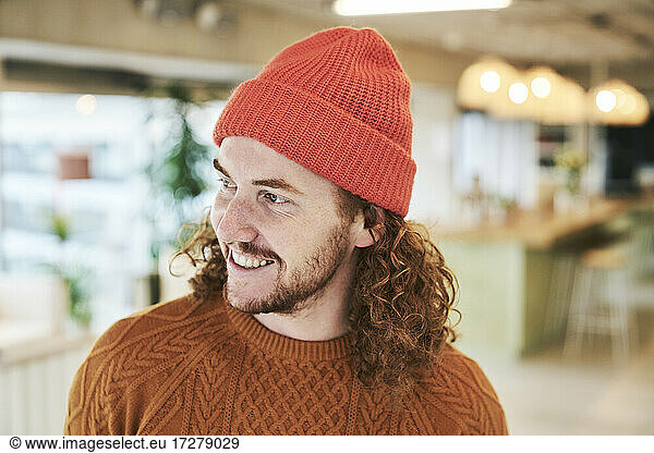 Lächelnder Hipster-Mann mit roter Strickmütze zu Hause