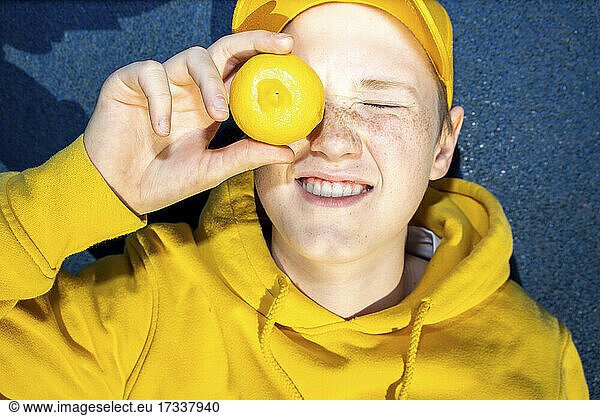 Lächelnder Junge bedeckt Auge mit Zitrone
