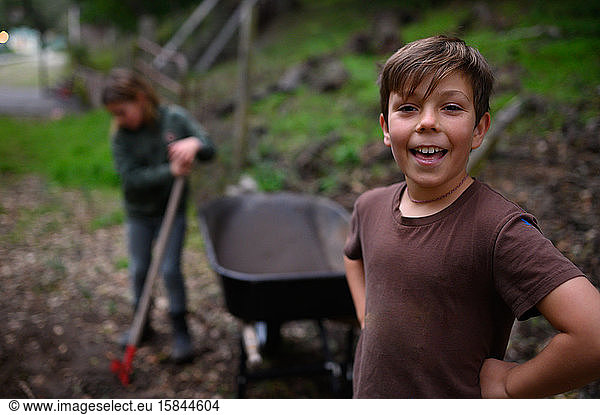 Lächelnder Junge in braunem T-Shirt steht neben Schubkarre im Hof