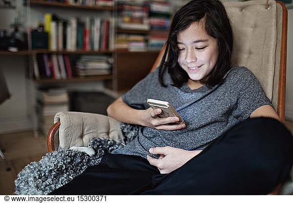 Lächelnder Junge nutzt soziale Medien auf einem Smartphone  während er zu Hause sitzt