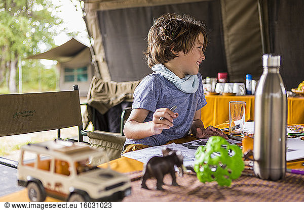 Lächelnder Junge  Profil  in einem Zeltlager  auf Safari  spielt mit Safari-Tierspielzeug.