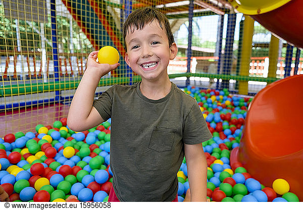 Lächelnder Junge wirft Ball in Ballgrube