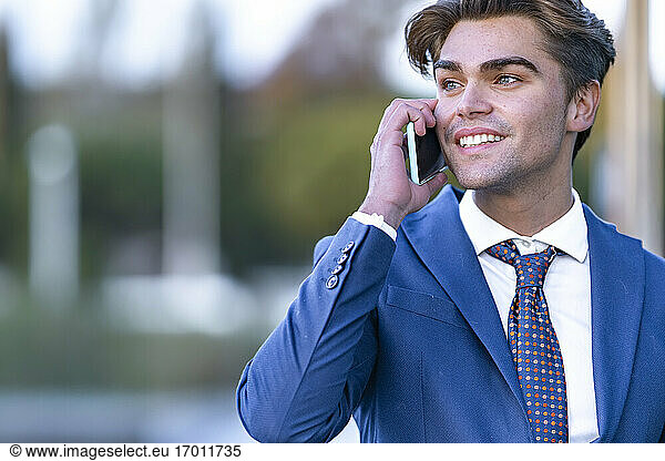 Lächelnder junger Geschäftsmann  der mit einem Mobiltelefon kommuniziert