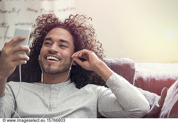 Lächelnder junger Mann  der mit Kopfhörern und mp3-Player Musik hört