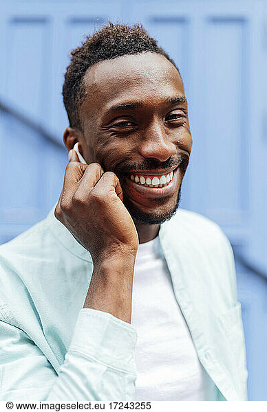 Lächelnder junger Mann in Freizeitkleidung mit In-Ear-Kopfhörern