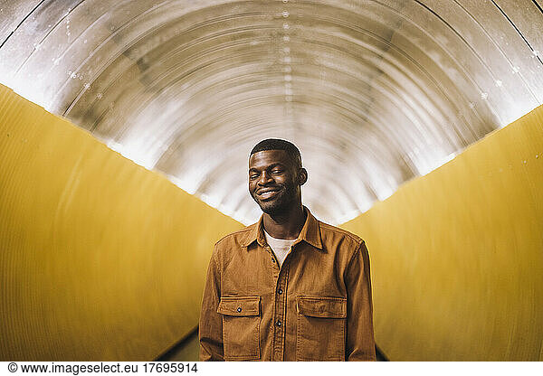 Lächelnder junger Mann mit geschlossenen Augen in einem U-Bahn-Tunnel stehend