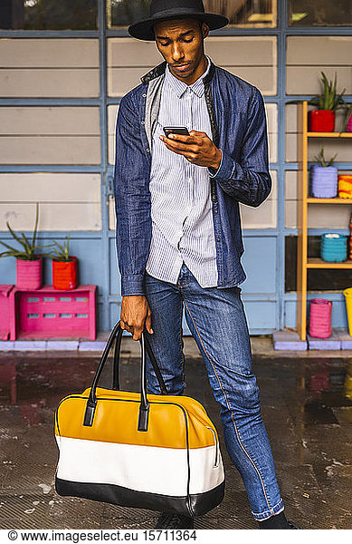 Lächelnder junger Mann mit Tasche mit Smartphone