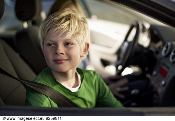 Lächelnder kleiner Junge  der durch das Autofenster schaut.