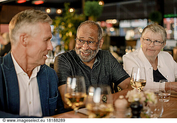 Lächelnder älterer Mann im Gespräch mit einem männlichen Freund  während er neben einer Frau im Restaurant sitzt