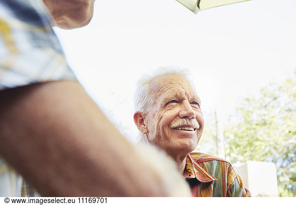 Lächelnder älterer Mann mit Schnurrbart sitzt in Gesellschaft im Freien.