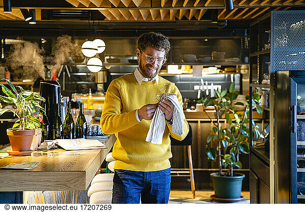 Lächelnder männlicher Café-Besitzer beim Reinigen von Weingläsern im Café
