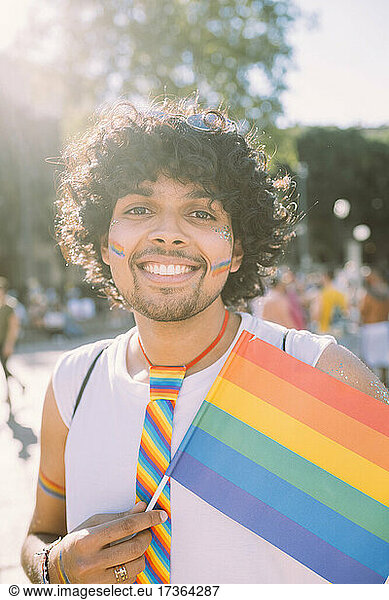 Lächelnder männlicher Demonstrant mit Regenbogenfahne bei einer Pride-Veranstaltung