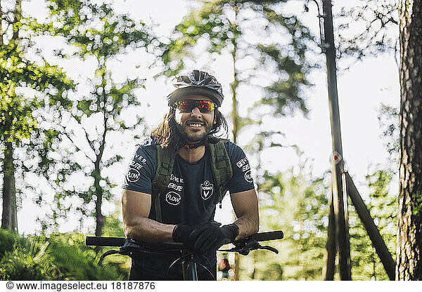 Lächelnder männlicher Radfahrer mit Helm  der sich auf sein Fahrrad stützt