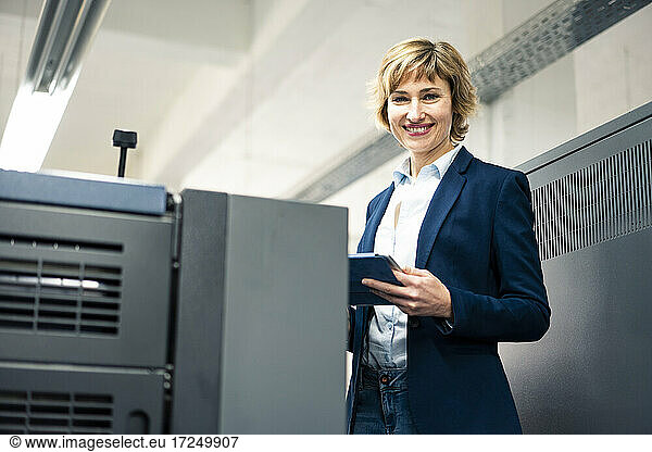 Lächelnder Manager mit digitalem Tablet an einer Druckmaschine