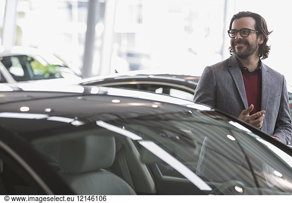 Lächelnder Mann beim Anschauen von Neuwagen im Autohaus