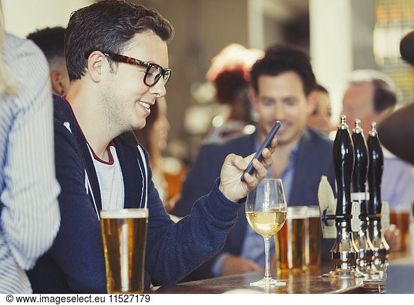 Lächelnder Mann beim SMSen mit Handy beim Weintrinken an der Bar
