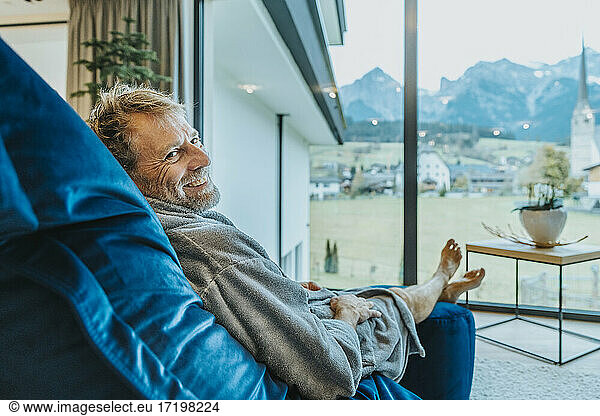 Lächelnder Mann entspannt sich auf einem Schaukelstuhl vor einem Fenster in einem Hotelzimmer