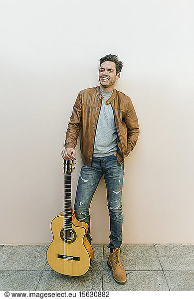 Lächelnder Mann mit Gitarre vor einer Wand