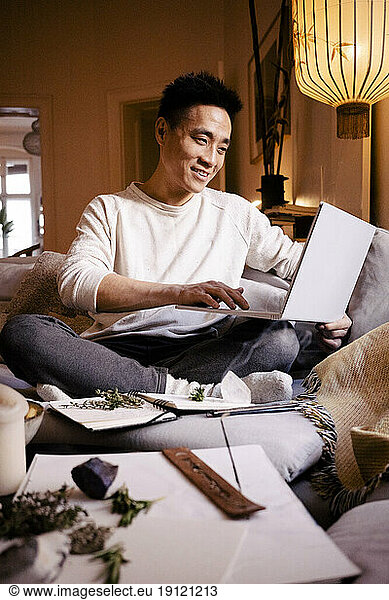 Lächelnder Mann mit Laptop auf dem Sofa im Wohnzimmer zu Hause