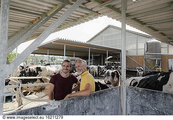 Lächelnder reifer Bauer mit erwachsenem Sohn im Kuhstall auf einem Bauernhof