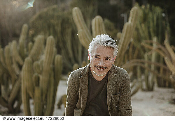 Lächelnder reifer Mann mit Kaktusgarten im Hintergrund