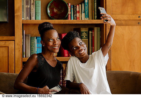 Lächelnder schwarzer Junge im Teenageralter  der ein Selfie mit seiner schönen Mutter Mitte 40 macht