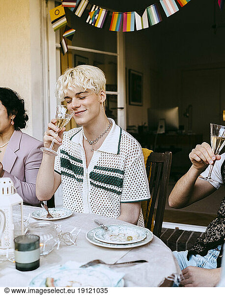 Lächelnder schwuler Mann  der an Wein riecht  während er bei einer Dinnerparty im Hinterhof am Tisch sitzt