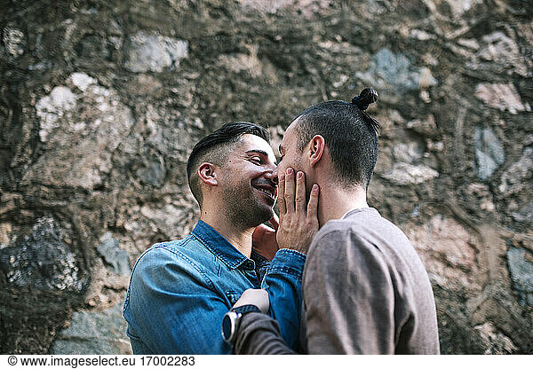 Lächelnder schwuler Mann  der seinen Freund an einer Steinwand betrachtet