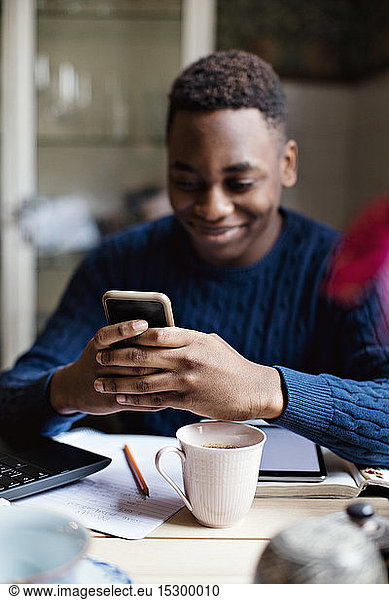 Lächelnder Teenager nutzt soziale Medien auf Smartphones beim Lernen zu Hause