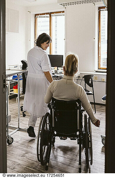 Lächelnder weiblicher medizinischer Experte  der eine behinderte Frau betrachtet  die in einer medizinischen Klinik zu Besuch ist