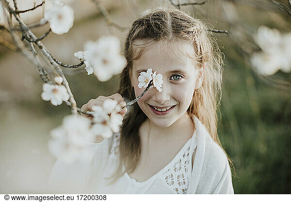 Lächelndes Mädchen hält einen Zweig einer Mandelbaumblüte im Frühling