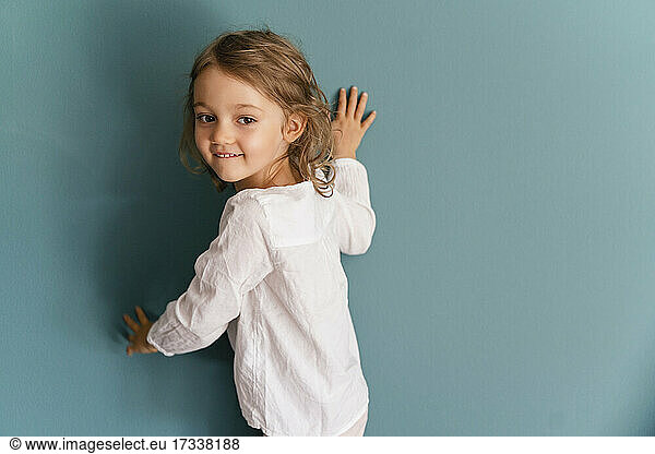 Lächelndes Mädchen lehnt an blauer Wand
