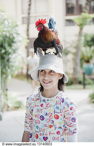 Lächelndes Mädchen mit Huhn auf dem Kopf auf der Straße stehend