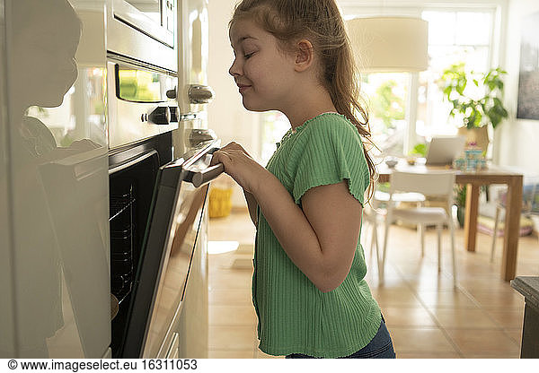 Lächelndes Mädchen schaut in den Ofen  während es in der Küche steht