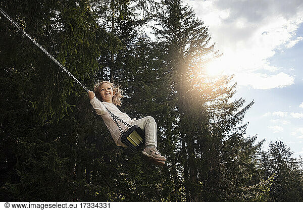 Lächelndes Mädchen schwingt auf einer Seilschaukel im Wald