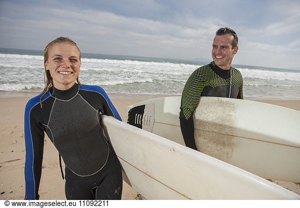 Lächelndes Paar mit Surfbrettern am Strand