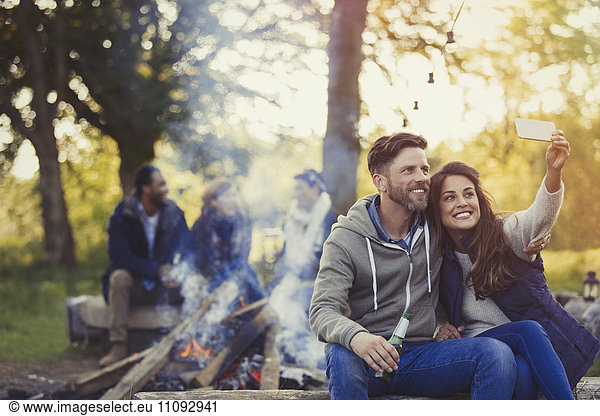Lächelndes Paar nimmt Selfie mit Fotohandy am Lagerfeuer mit.