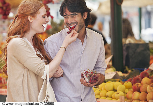 Lächelndes Paar schmeckt Obst auf dem Markt