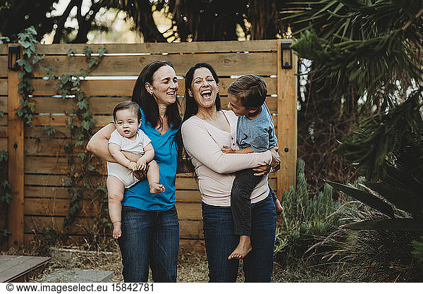 Lachende Familie mit zwei Müttern und zwei Kindern im Hinterhof beim Zaun